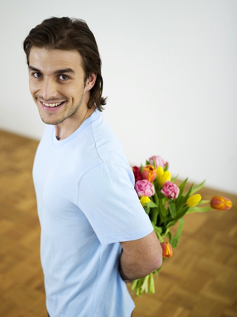 Young man hiding bunch of flowers behind his back