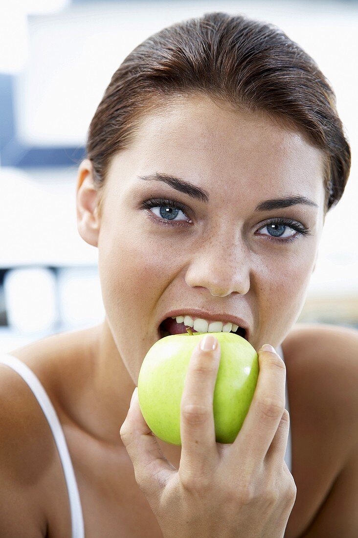 Young woman biting into a green apple