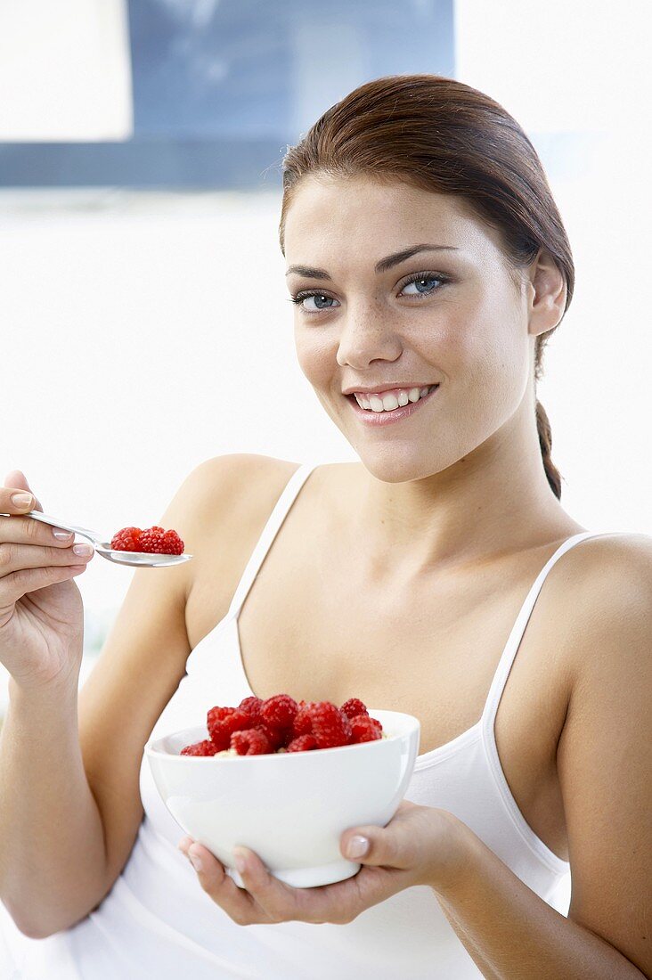 Young woman holding bowl of fresh rasberries