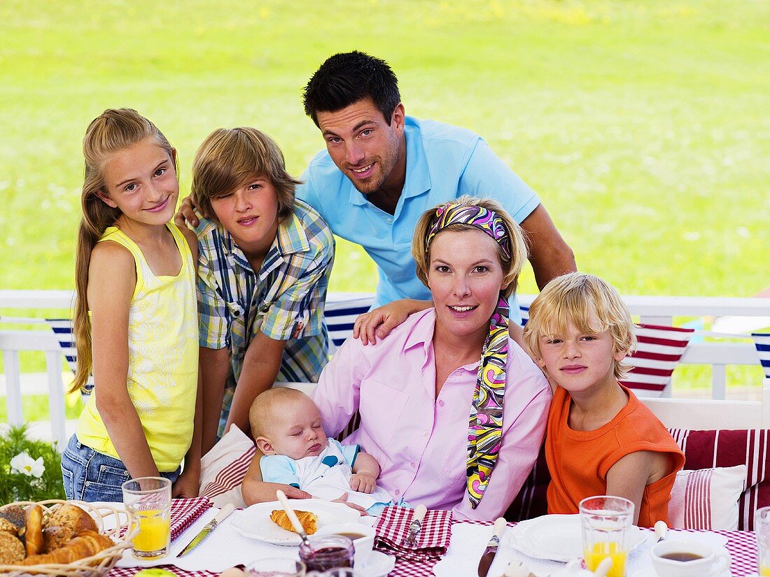 Familie mit Baby am Frühstückstisch im Garten