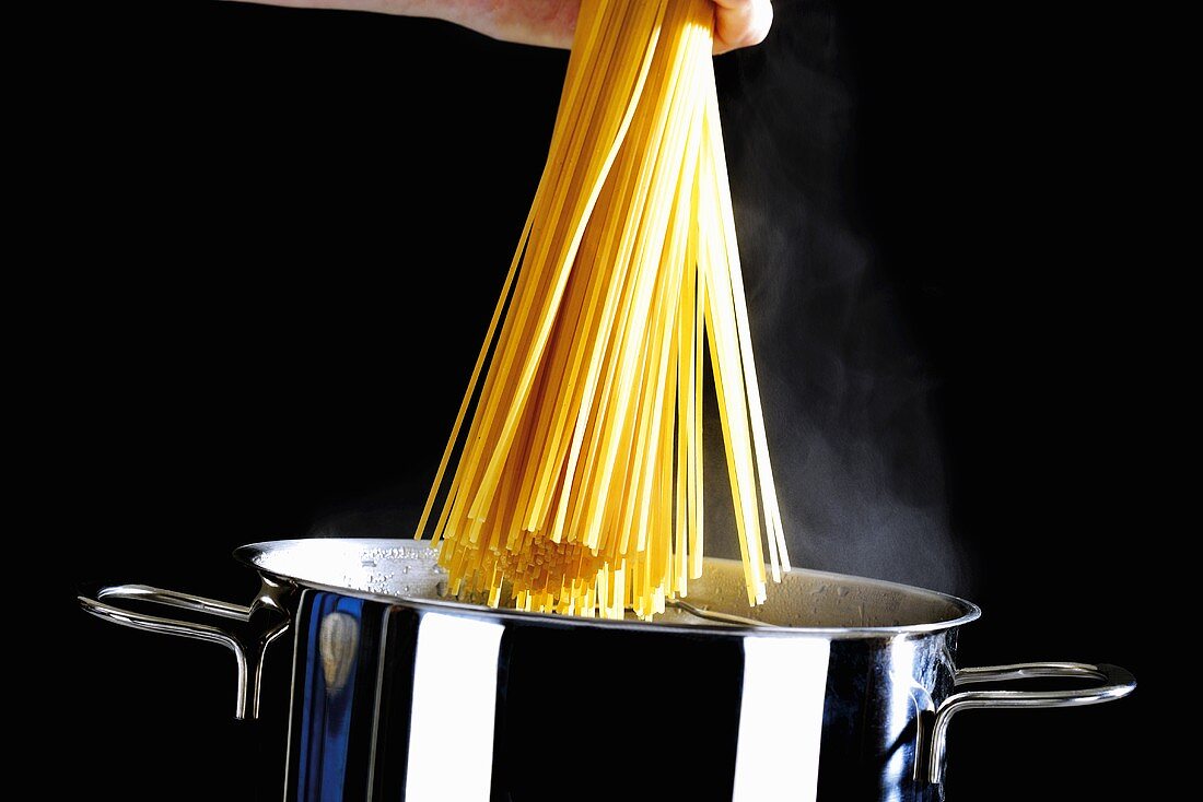 Hand hält Spaghetti über dampfendem Kochtopf