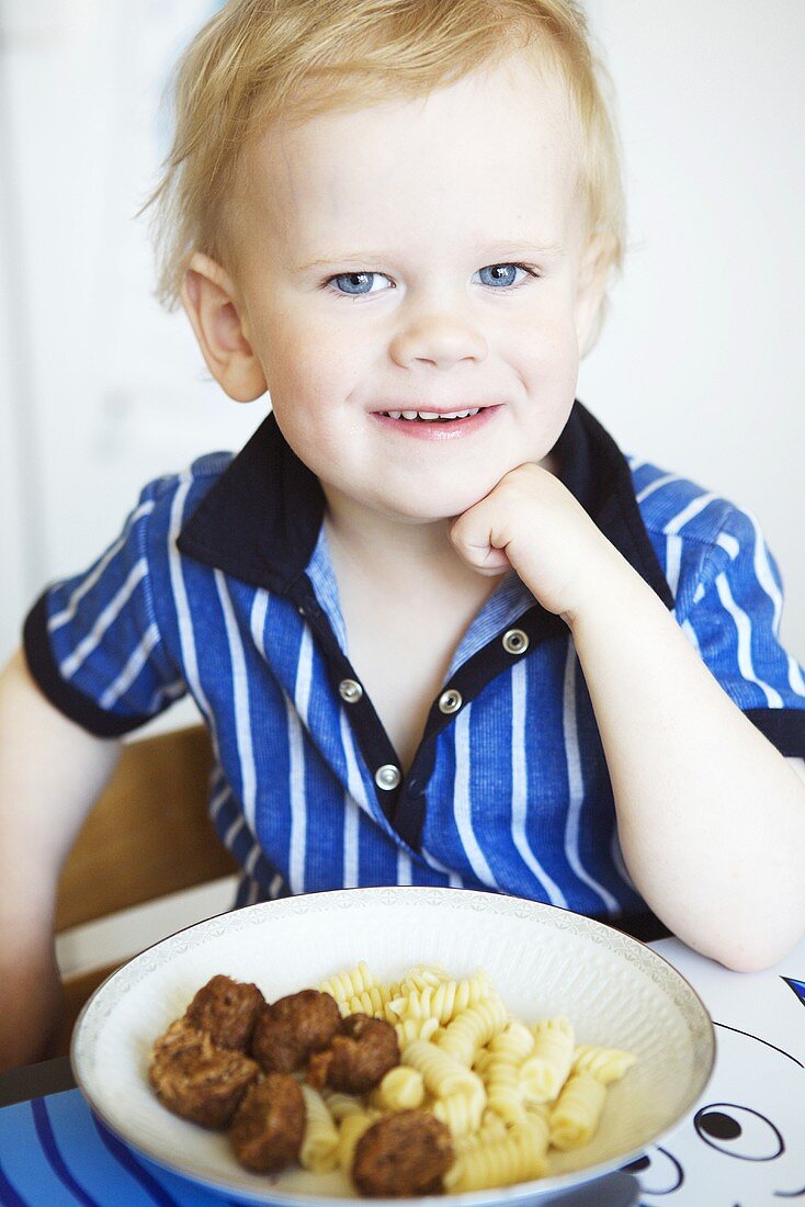 Boy sitting in front of plate of meatballs and pasta