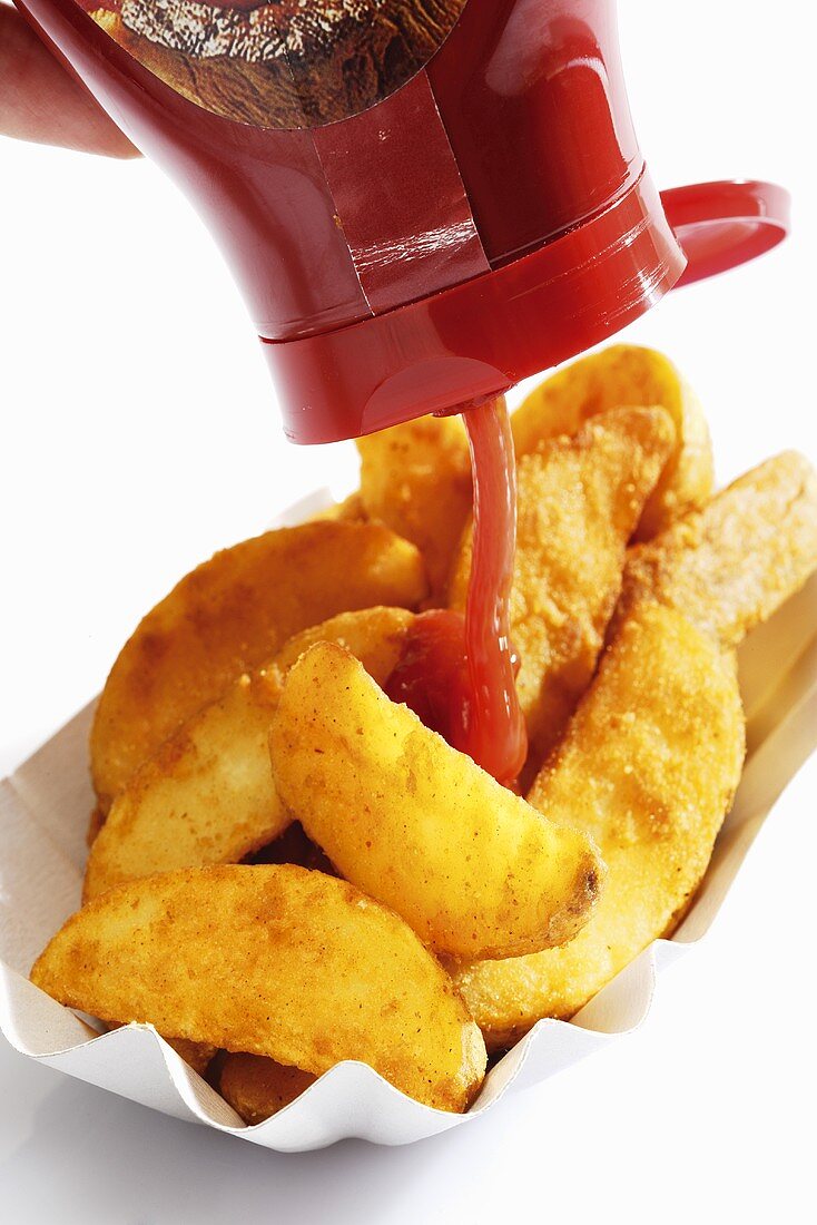 Ketchup being poured on potato wedges