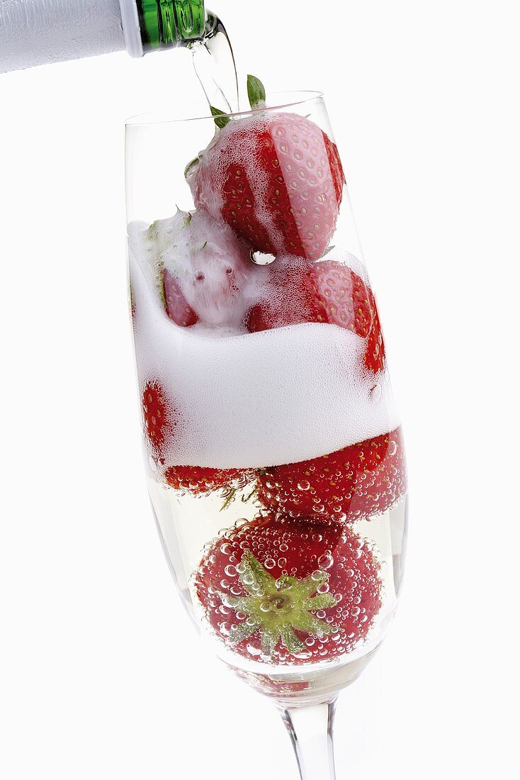 Sekt in Glas mit Erdbeeren gießen