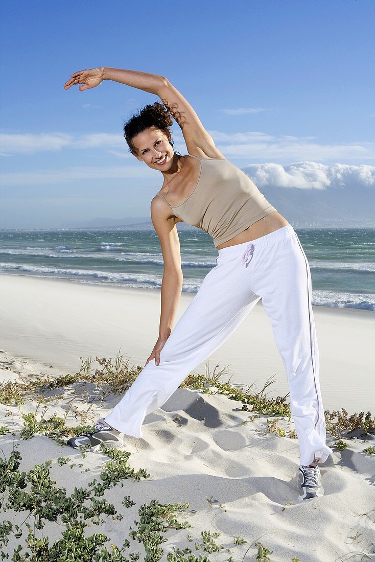 South Africa, Cape Town, Young woman stretching on beach