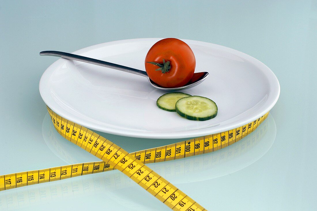Tomato and cucumber slice on plate with measuring tape, close-up
