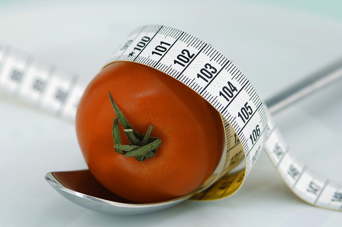 Tomate auf Löffel, mit Massband umwickelt (Nahaufnahme)