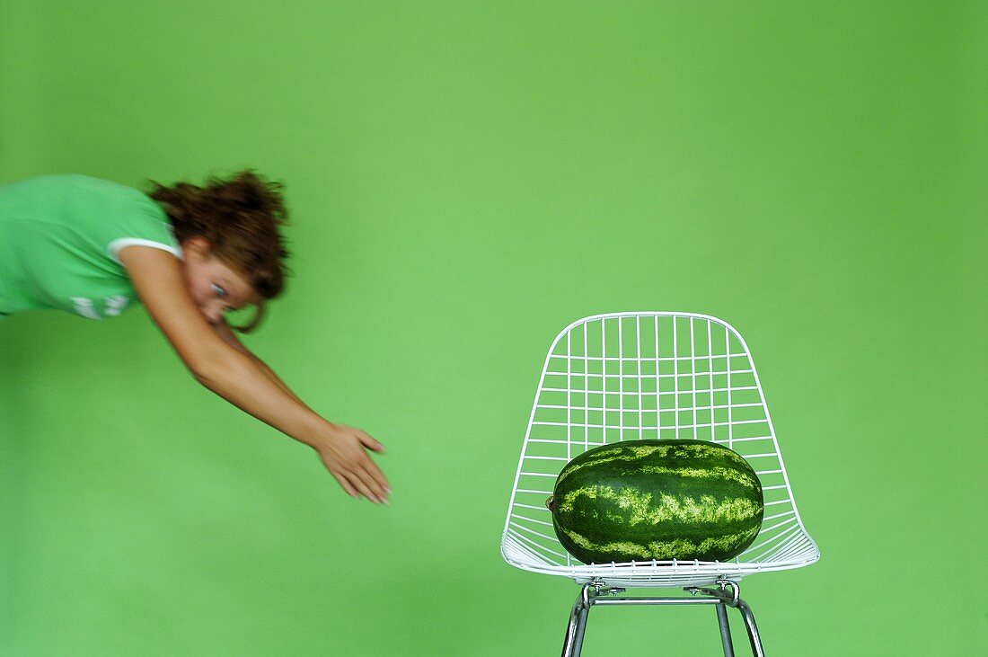 Young woman exercising by watermelon on chair, (blurred motion)