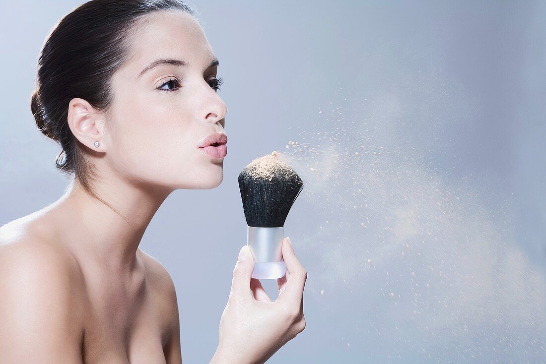 Young woman holding makeup brush, blowing, portrait