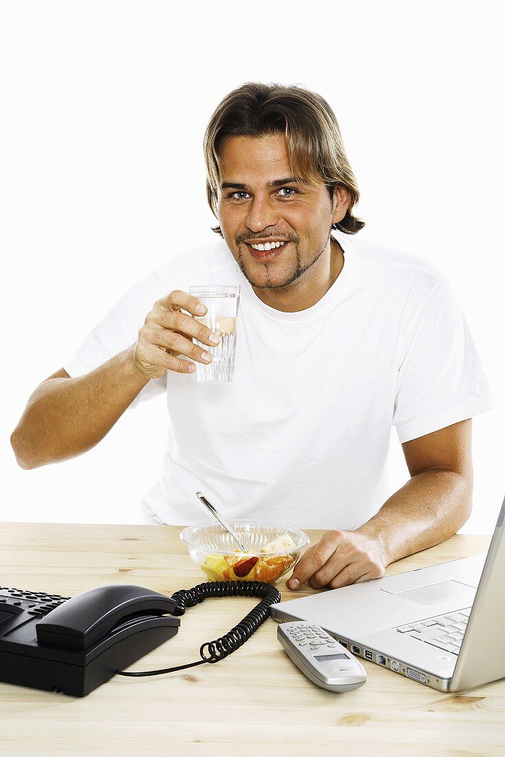 Junger Mann trinkt Wasser am Schreibtisch sitzend