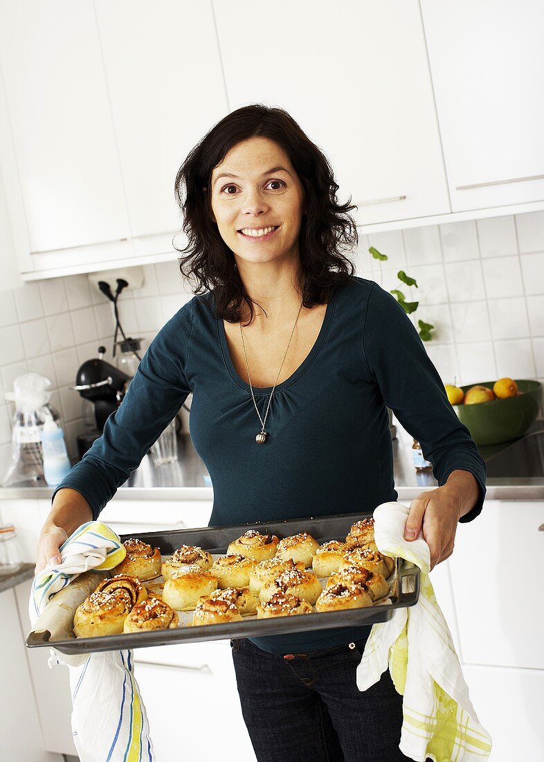 Woman holding a baking tray of cinnamon buns