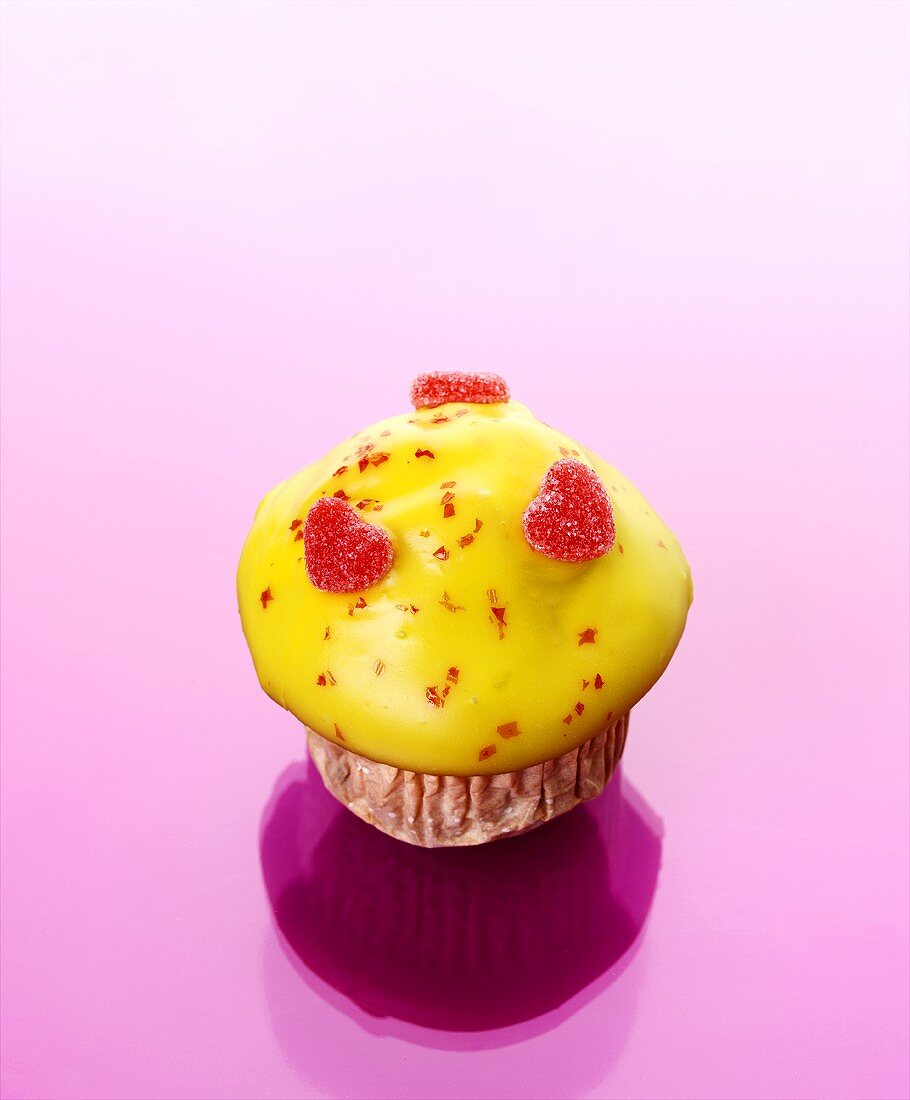 Muffin mit gelbem Zuckerguss und Fruchtgummi-Herzen