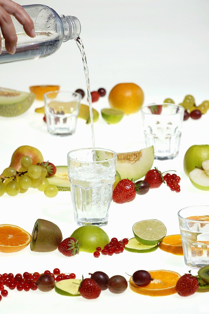 Hand pouring water into glass, fresh fruits