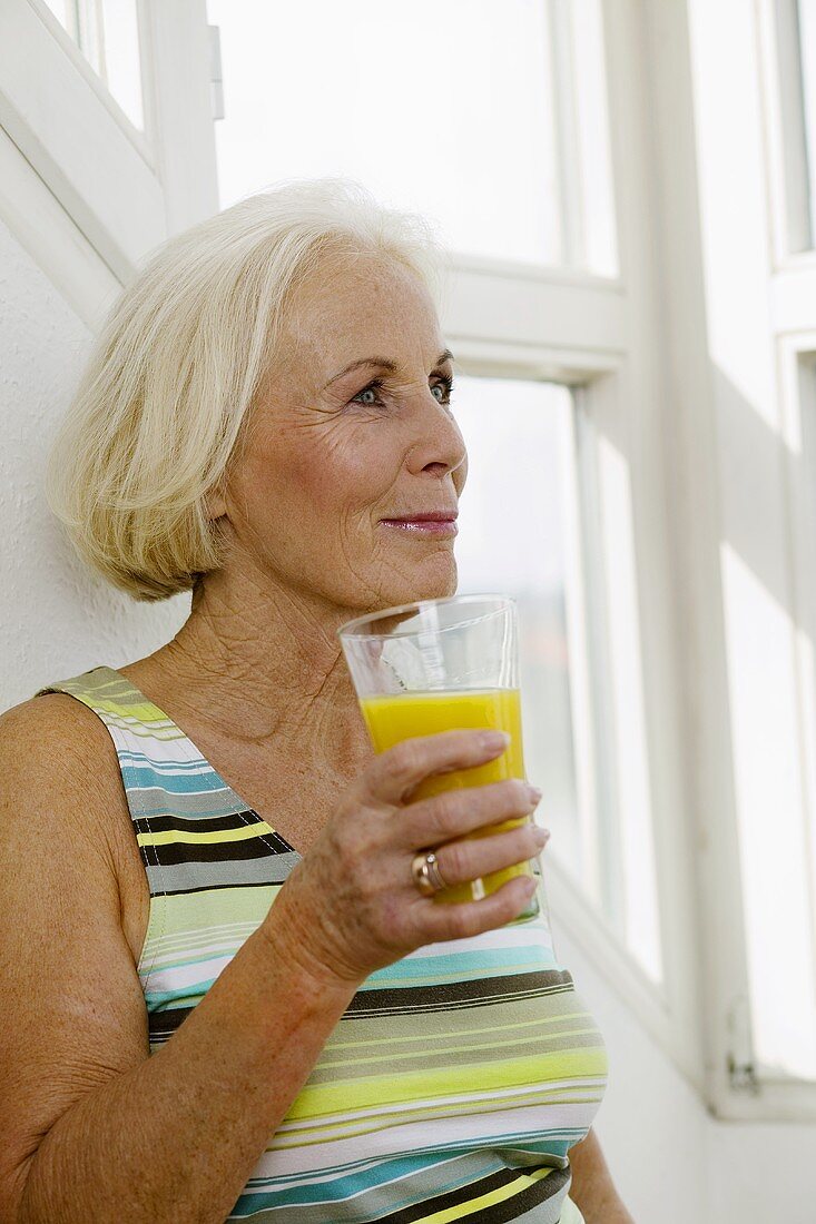 Senior woman holding glass of juice, smiling, close-up