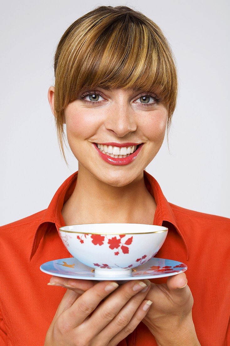 Young woman holding tea bowl, smiling, close-up