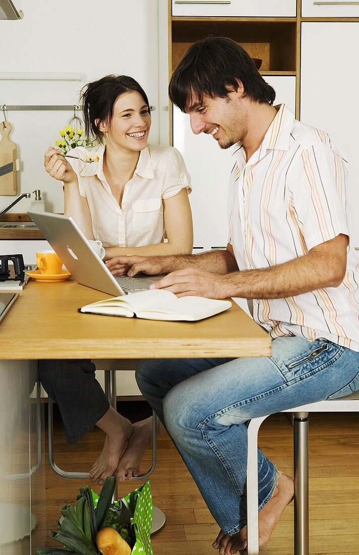 Young couple in kitchen, man using laptop, smiling