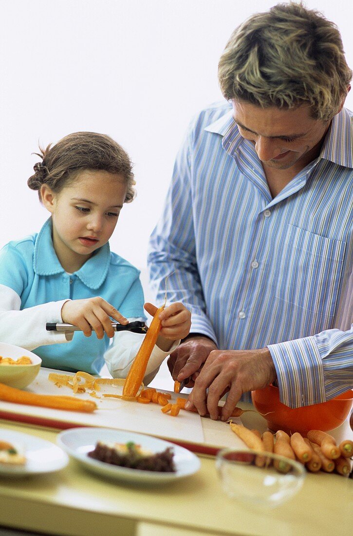 Father and daughter (4-7) peeling carrot, close-up