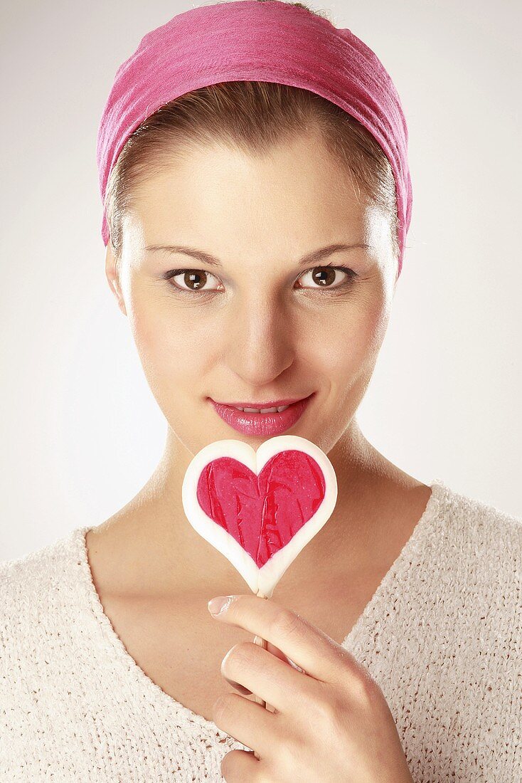 Young woman holding heart shaped lollipop, close-up, portrait