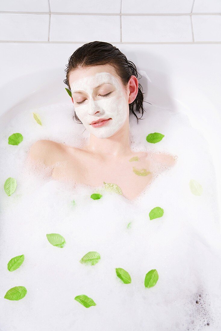 Young woman with face mask taking a bubble bath, eyes closed