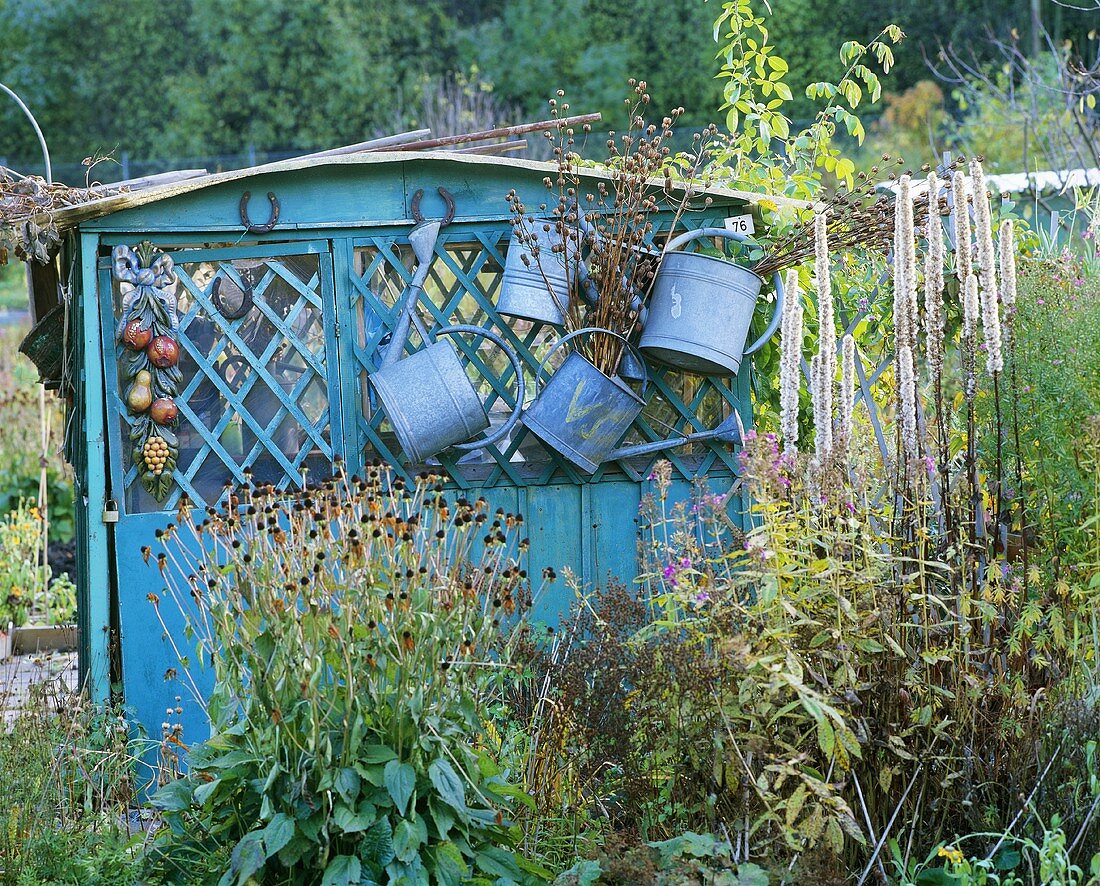 Hängende Giesskannen an einer Gartenlaube im herbstlichen Garten