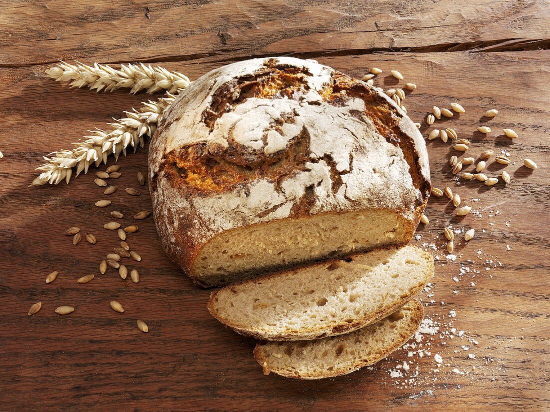 Rustic loaf of bread, partly sliced, ears & grains of wheat