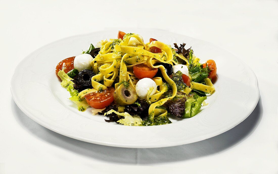 Pasta with pesto on salad leaves with olives, mozzarella and tomatoes