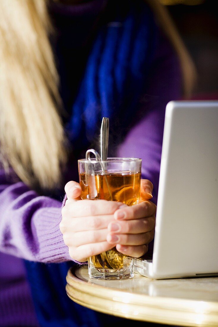 Frau wärmt sich die Hände an einem Glas Tee