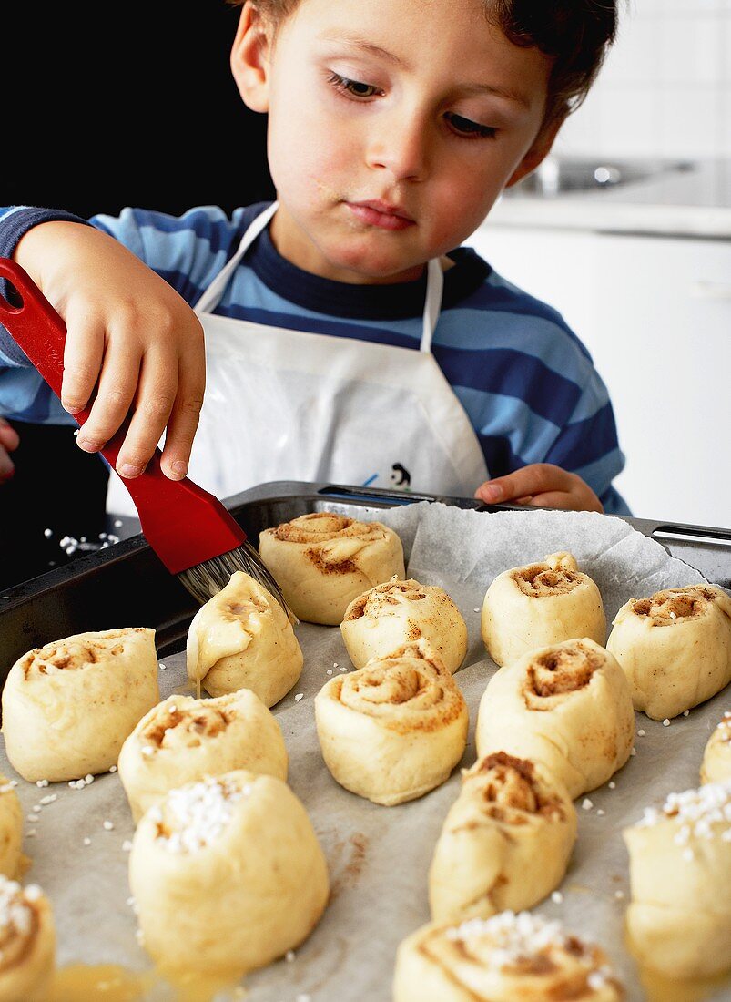 Little boy brushing cinnamon buns with butter