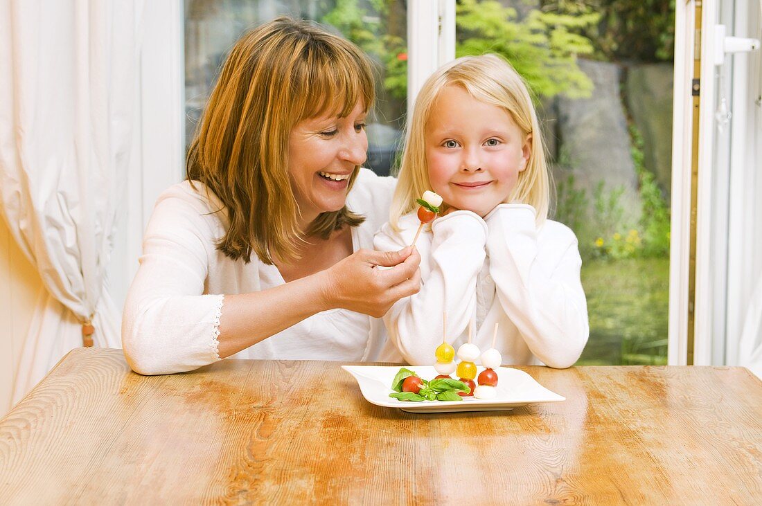 Mutter und Tochter essen Tomaten-Mozzarella-Spiesschen