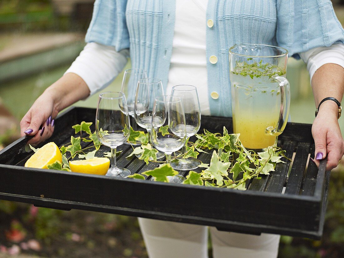 Frau trägt Tablett mit Limonade und Gläsern