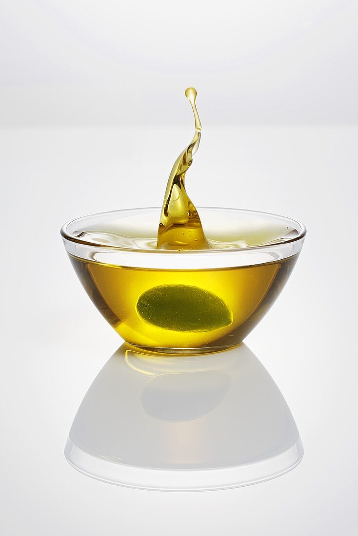 Green olive falling into glass dish of olive oil