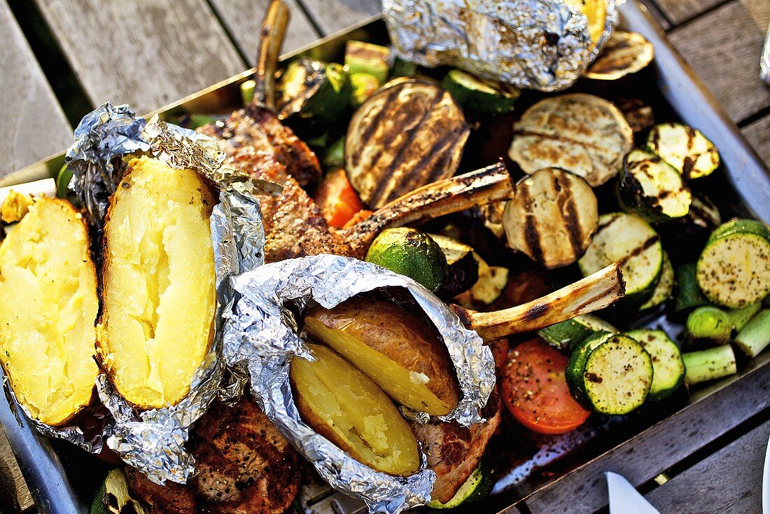 Barbecued vegetables, baked potatoes, lamb chops on barbecue tray