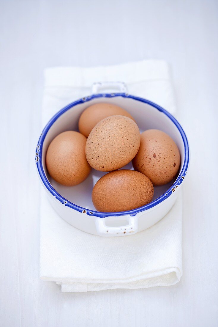 Several brown eggs in pan on tea towel