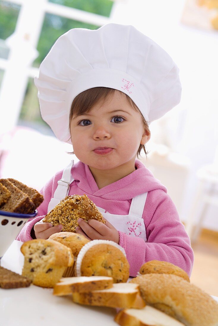 Kleines Mädchen mit Kochmütze sitzt am Tisch vor Muffins