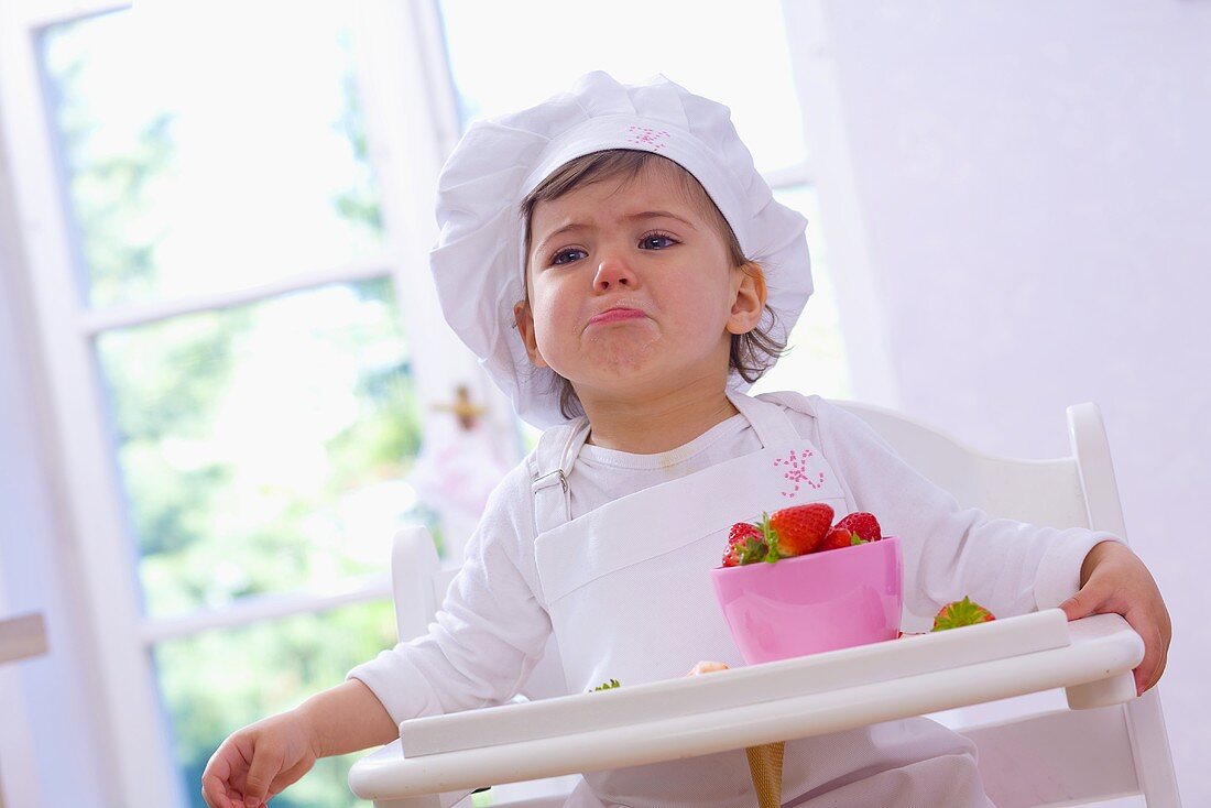 Little girl in chef's hat eating strawberries