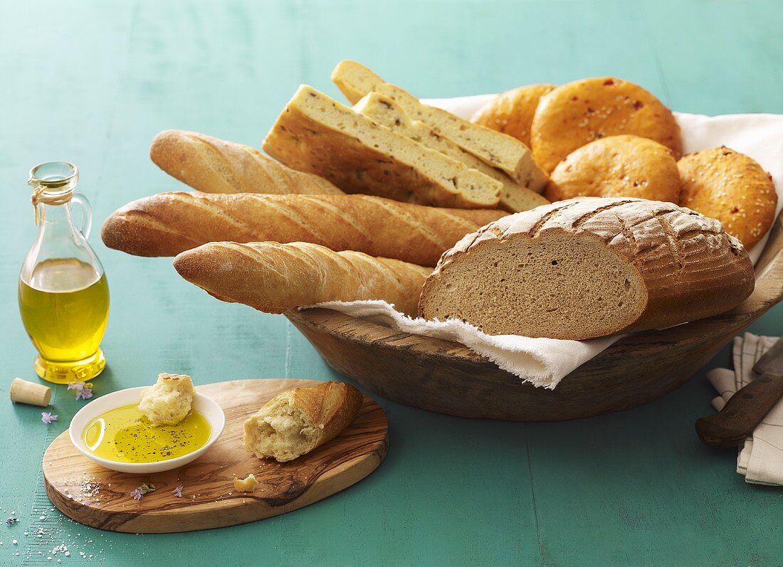 Assorted bread and bread rolls in bread basket, olive oil beside it