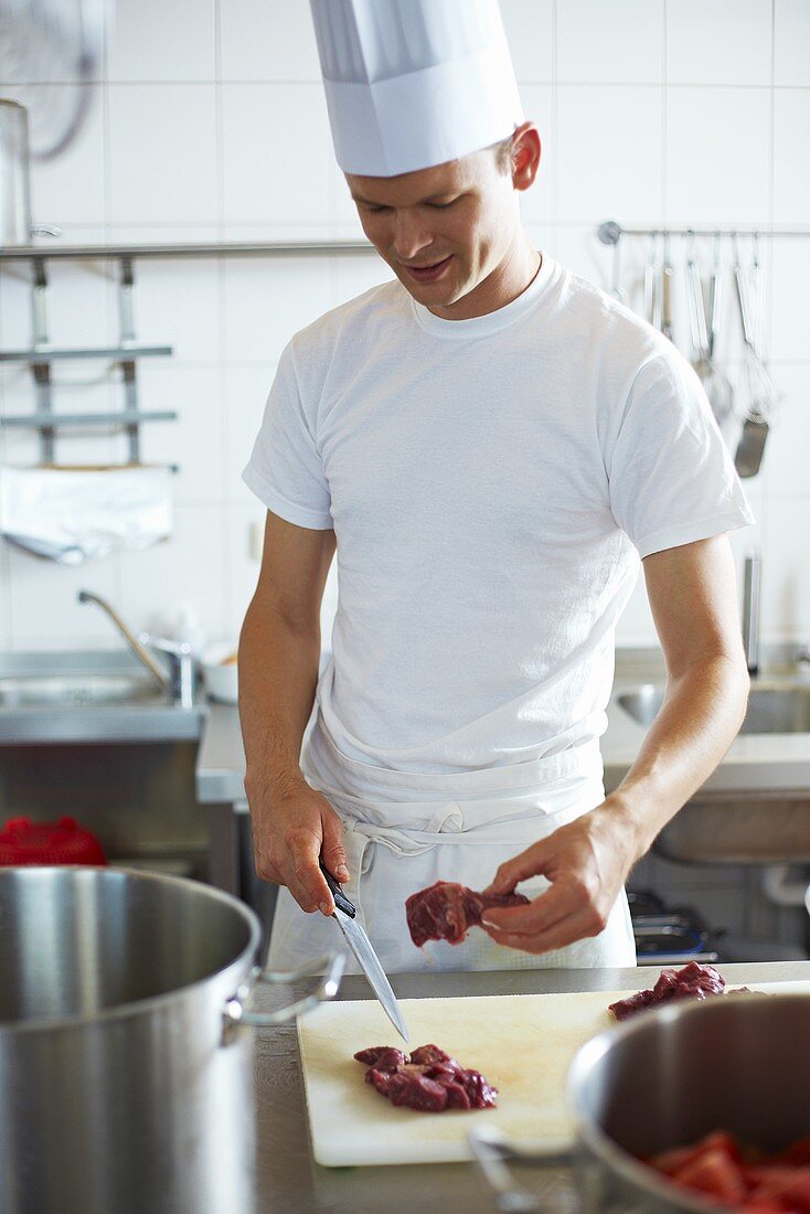 Young chef cutting up beef