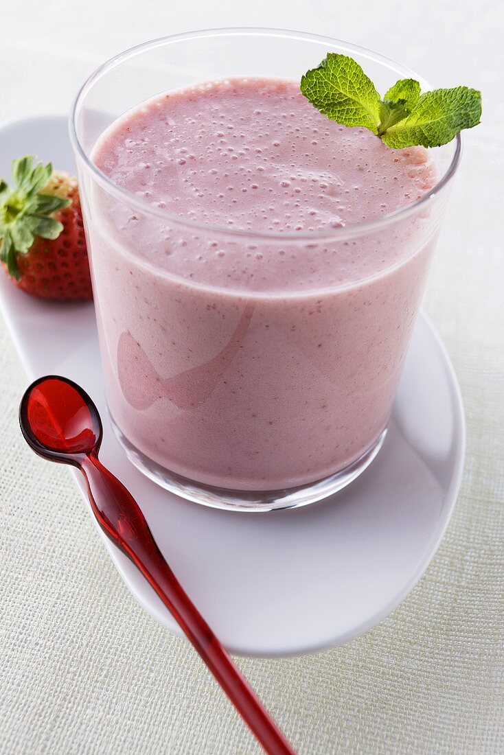 Strawberry smoothie in glass on plate with spoon and fresh strawberry