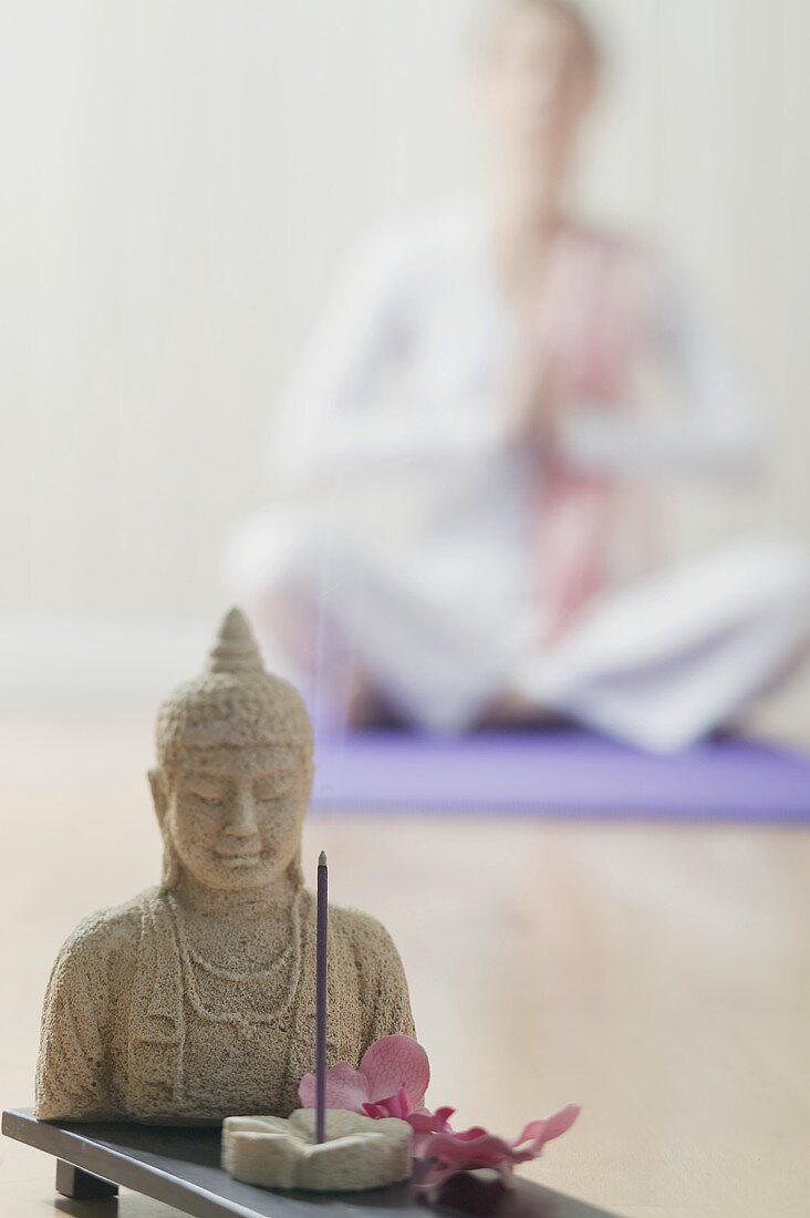 Buddhastatue und Räucherstäbchen, dahinter Frau im Yogasitz
