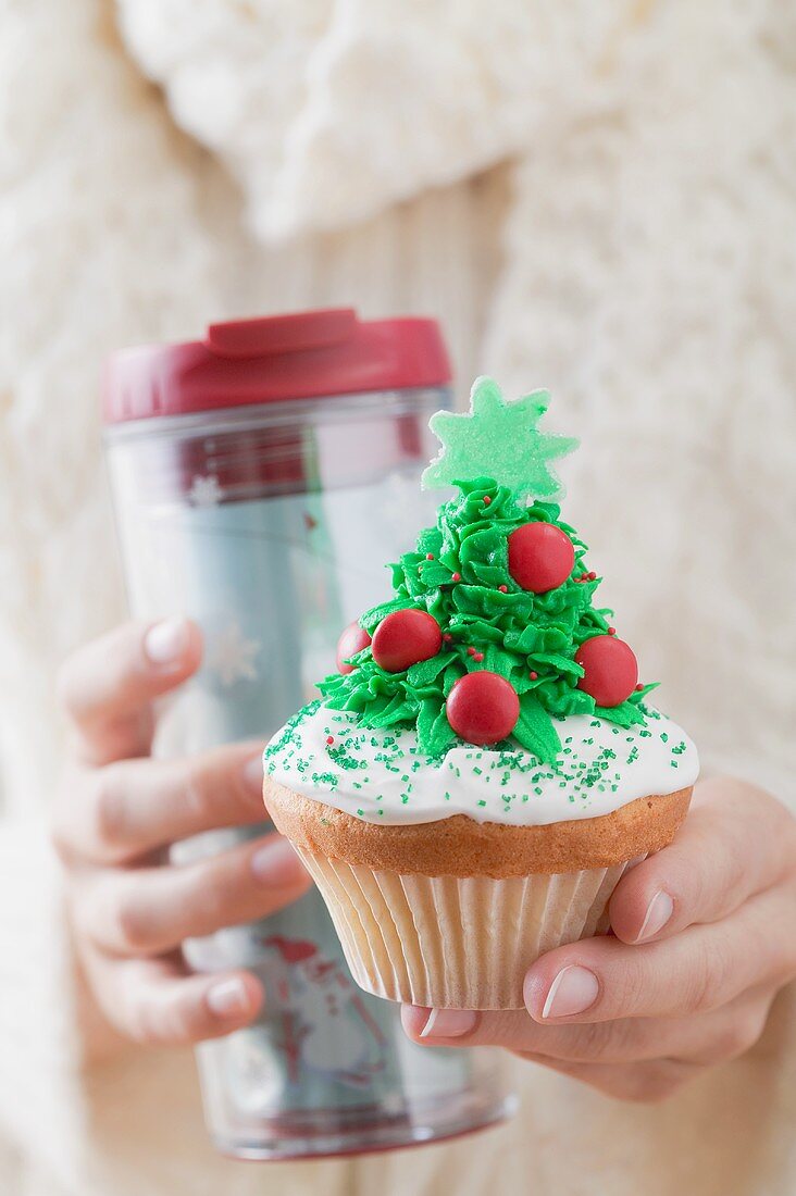 Frau hält Cupcake und Thermobecher zu Weihnachten