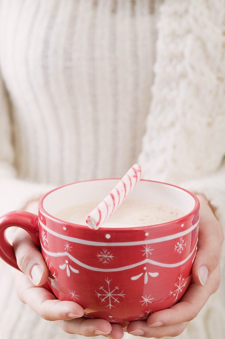 Frau hält Tasse Kakao mit Zuckerstange (weihnachtlich)