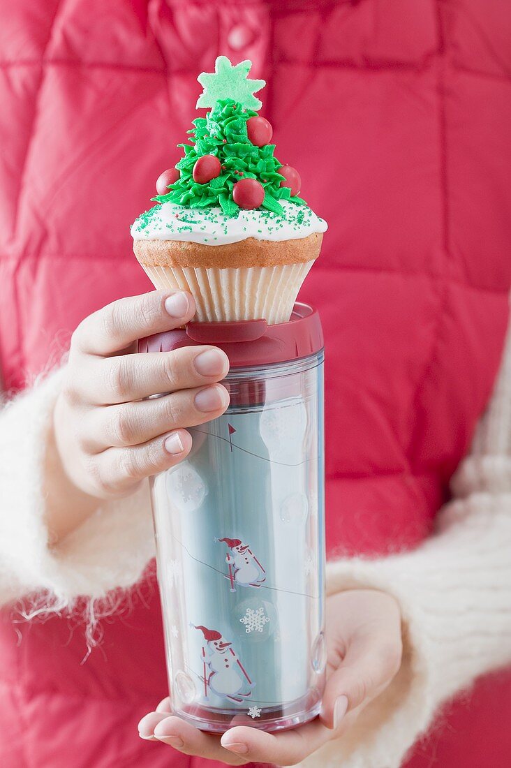 Frau hält Cupcake auf Thermobecher zu Weihnachten