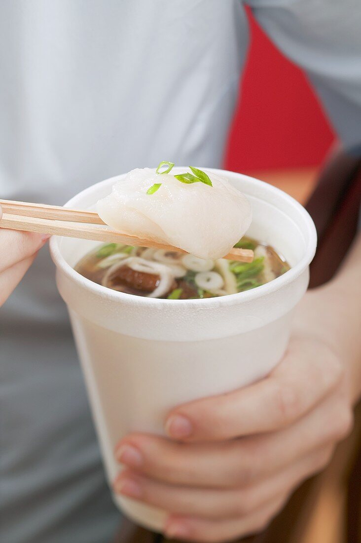 Woman holding paper cup of Asian noodle soup