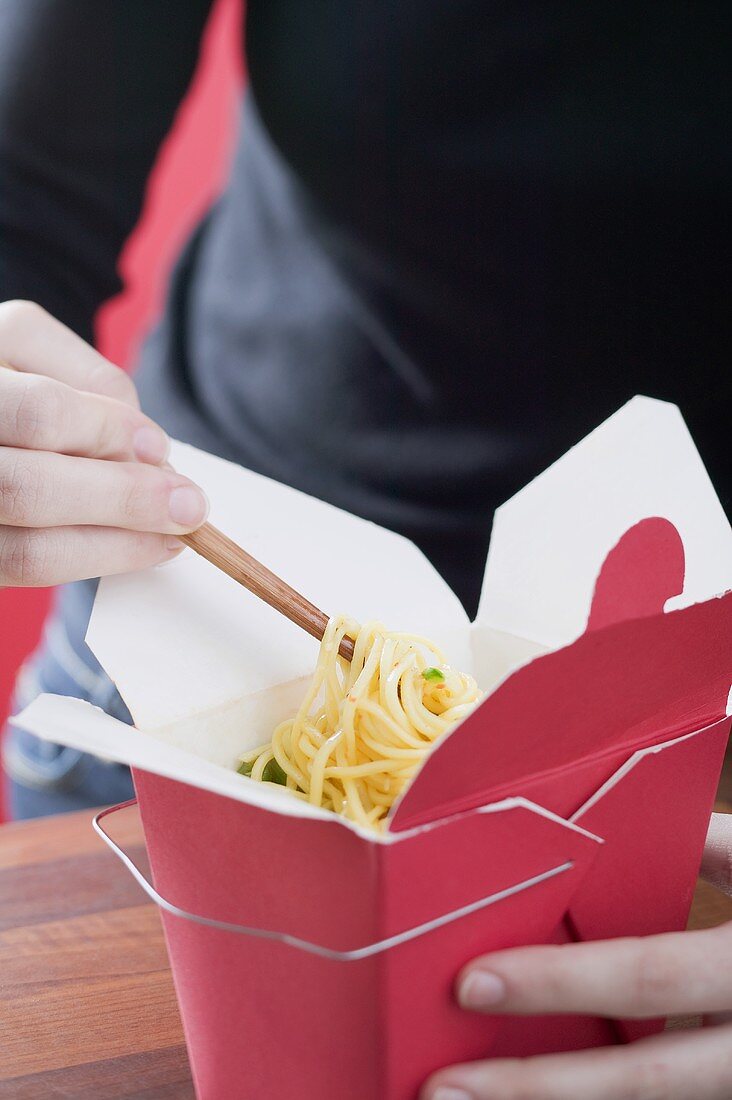 Person eating Asian noodle dish out of take-away container