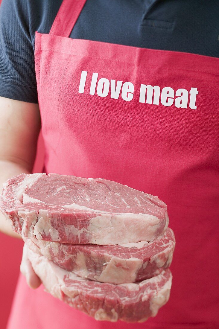 Man in apron holding three beef steaks