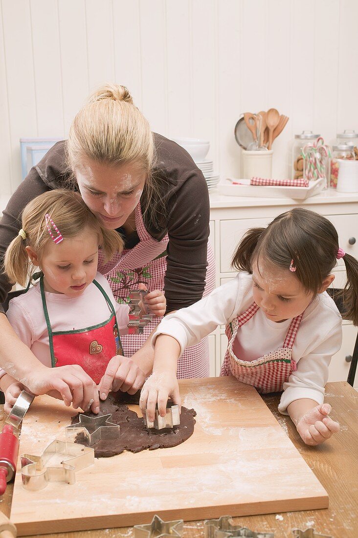Frau und zwei kleine Mädchen stechen Schokoladenplätzchen aus