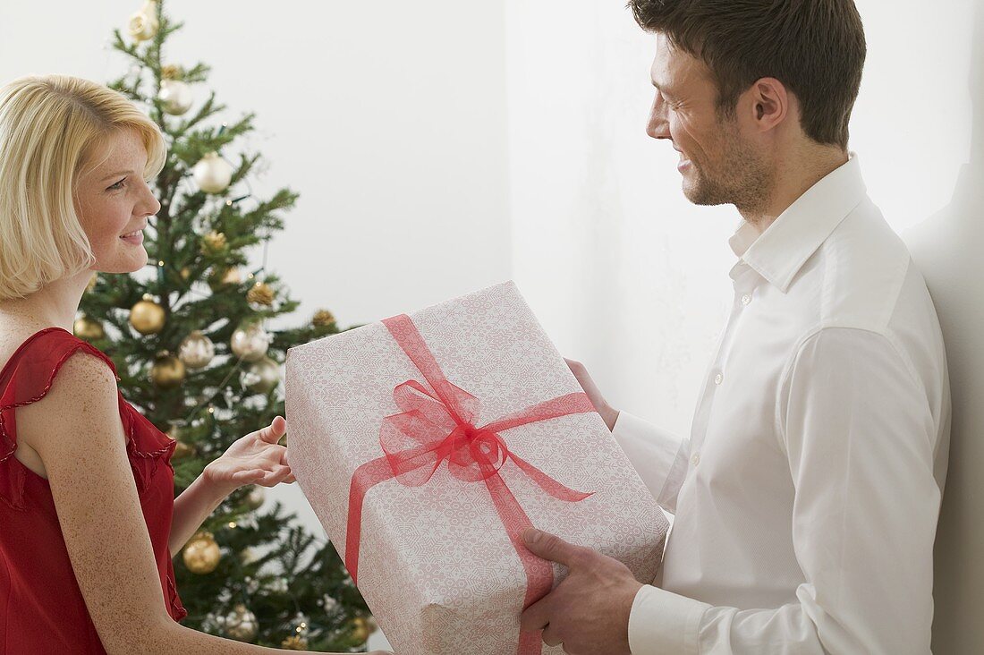 Paar mit Weihnachtsgeschenk vor Christbaum