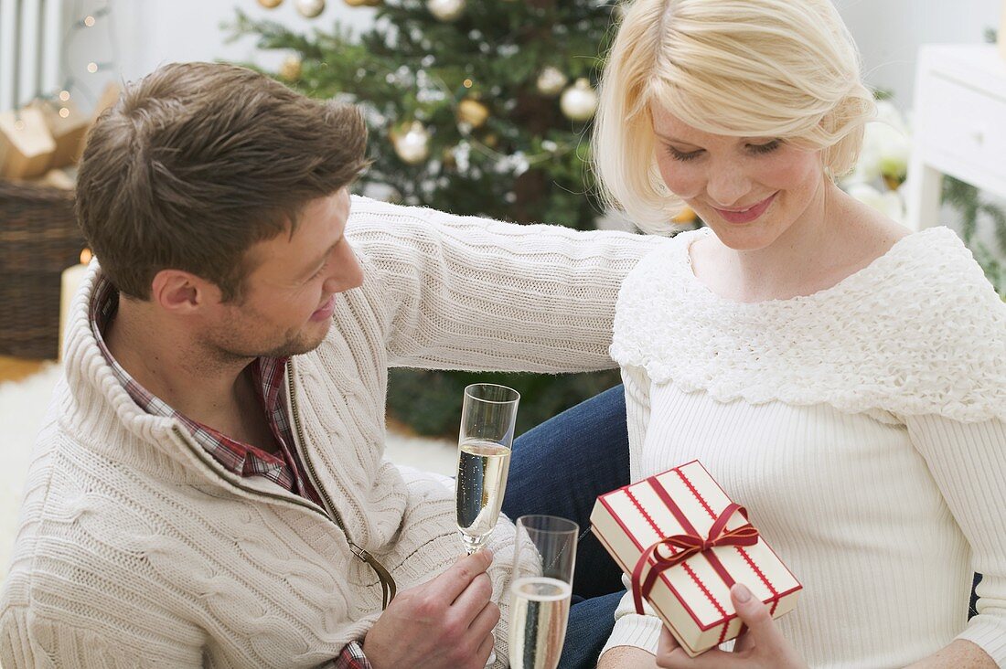 Mann und Frau halten Sektgläser und Weihnachtsgeschenk