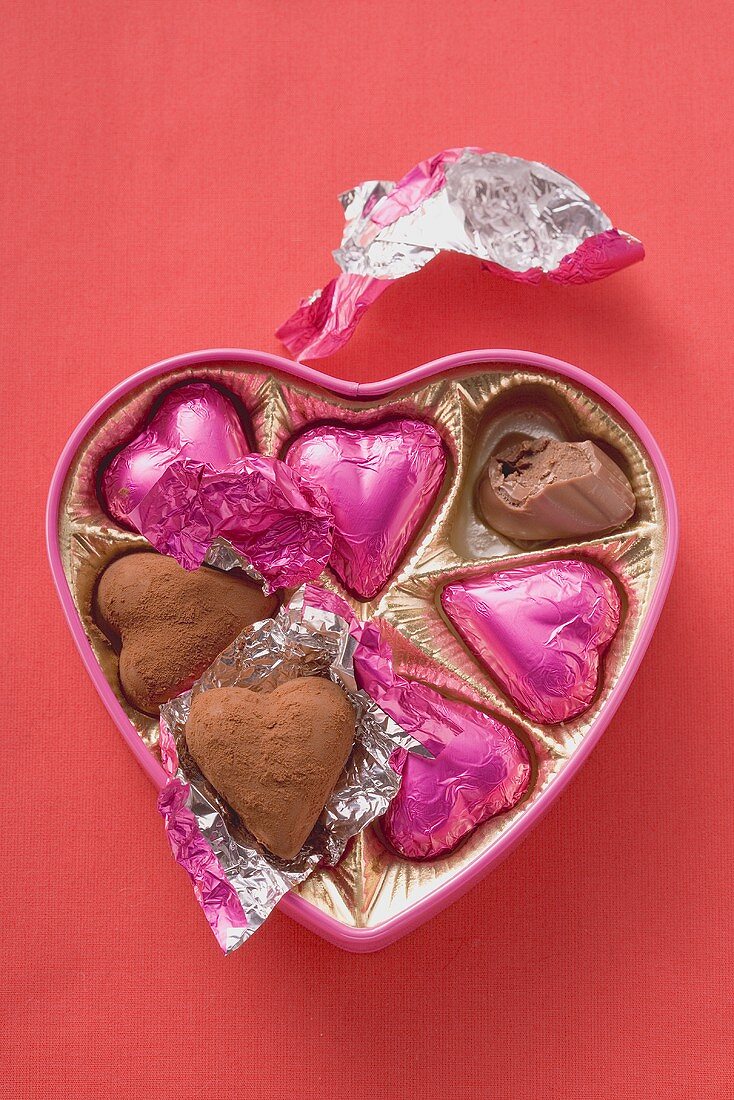 Pink chocolates in heart-shaped box (one partly eaten)