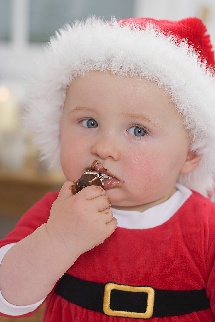 Baby in Father Christmas hat eating chocolate